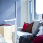 A woman talking on the phone while sitting on a sofa with an Advantage rail floor-mounted grab bar and support next to her.