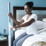 A woman using an Advantage rail floor-mounted grab bar and support to easily stand from a bed.