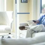 A superpole with superbar is installed next to a sofa to help a man sit and stand safely.