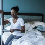 A woman is using the Superpole with Superbar to get up and out of bed.