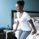 A woman leans on the HealthCraft Smart Rail as she stands up from her bed.