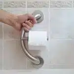 Hand holding onto a PLUS Brushed Toilet Roll Holder for support